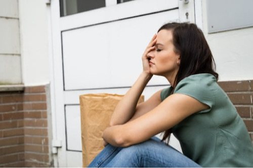 die frau sitzt vor dem haus und hält sich den kopf